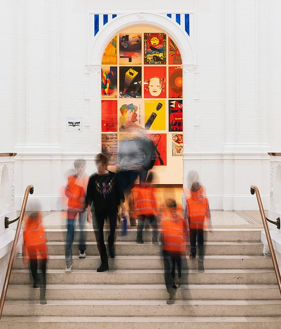 Visitors descending the gallery steps beneath a wall of framed works